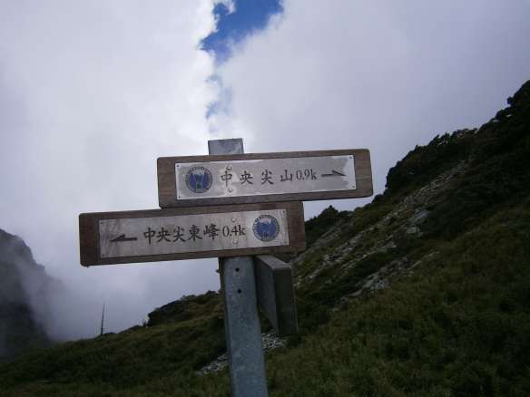A signpost marks the saddle at the top of the scree slope.